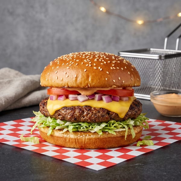A cheeseburger with lettuce, tomato, onion, and special sauce on a red and white checkered paper.
