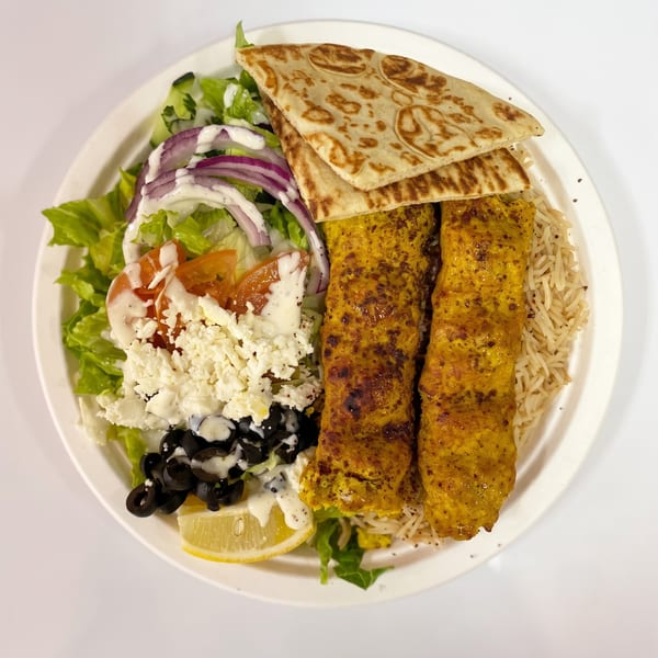 A plate of chicken kabobs with rice, salad, feta, olives, red onion, and pita bread.