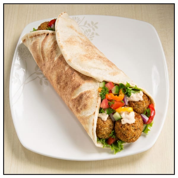 A falafel wrap with lettuce, tomatoes, cucumbers, bell peppers, and sauce on a white plate.