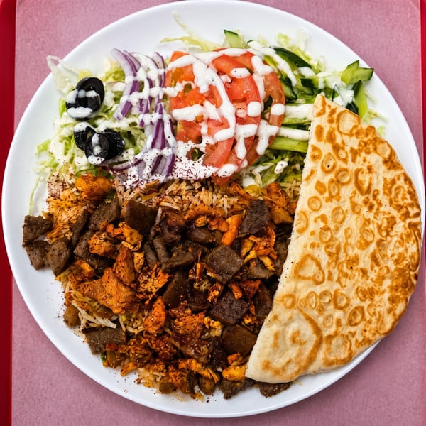A white plate with rice, meat, salad, and a piece of naan bread, drizzled with white sauce.