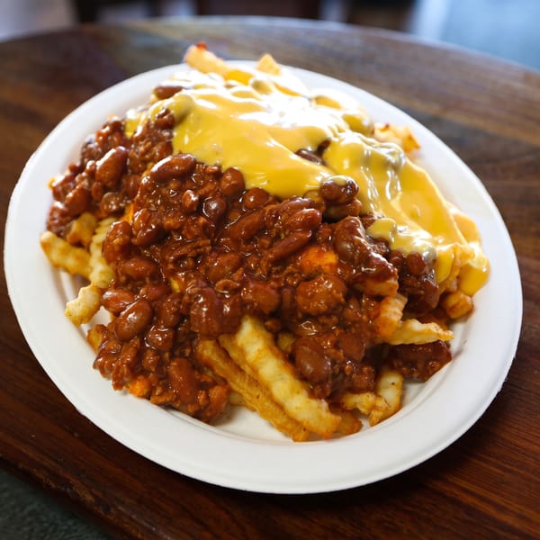 A white plate holds a generous serving of chili cheese fries on a wooden table.